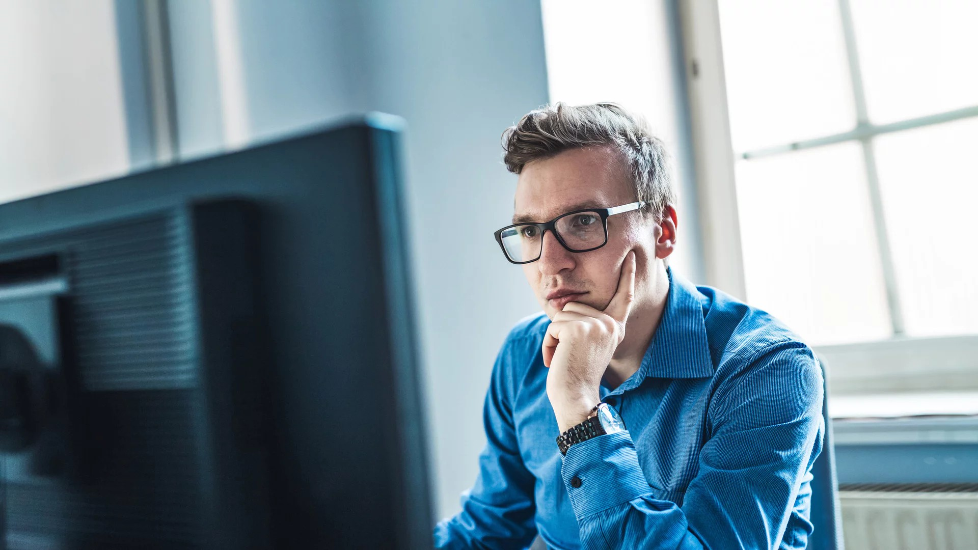 Mann mit Brille sitzt vor einem Bildschirm. 